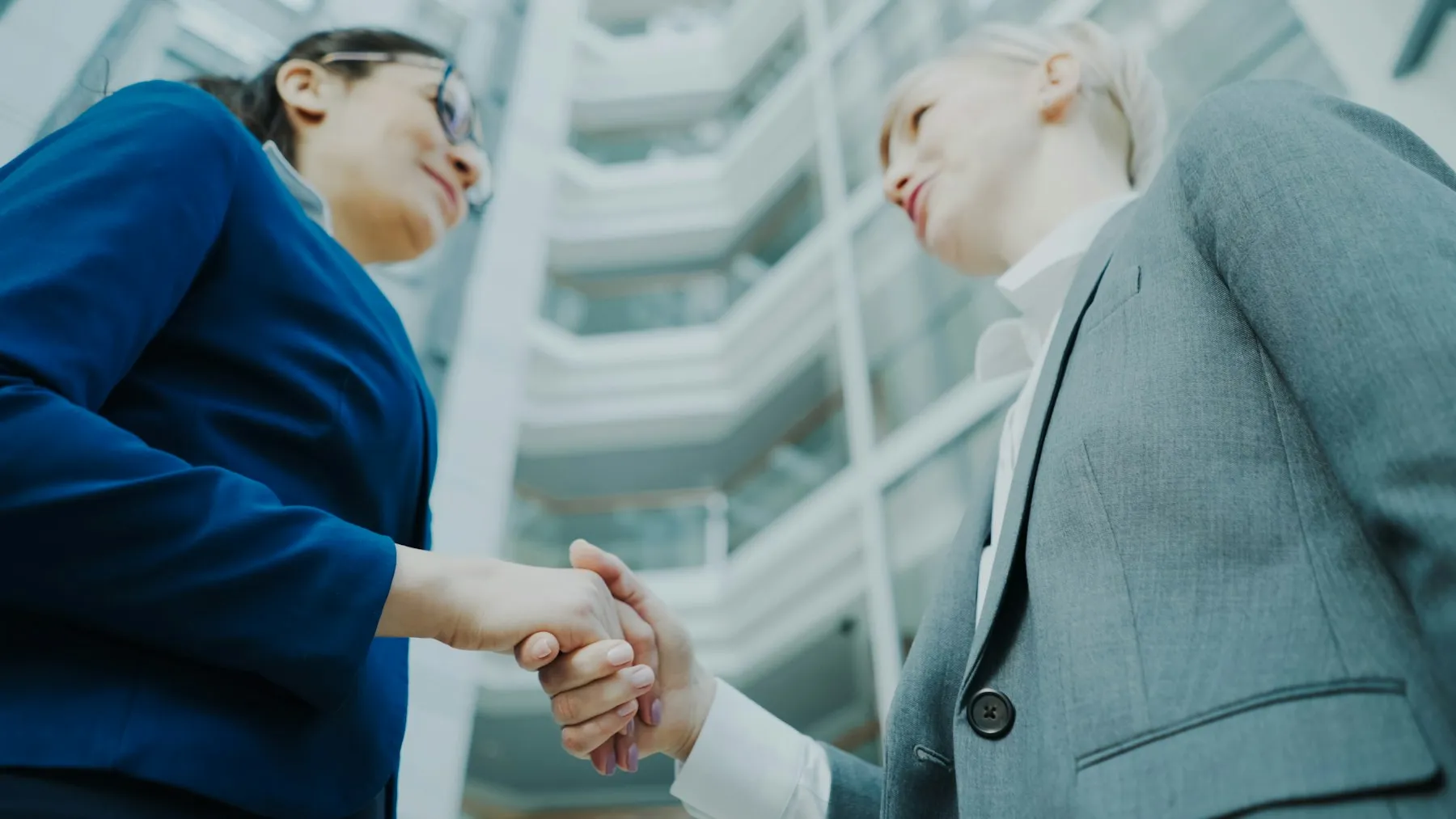 Two professionals shaking hands in a modern office atrium