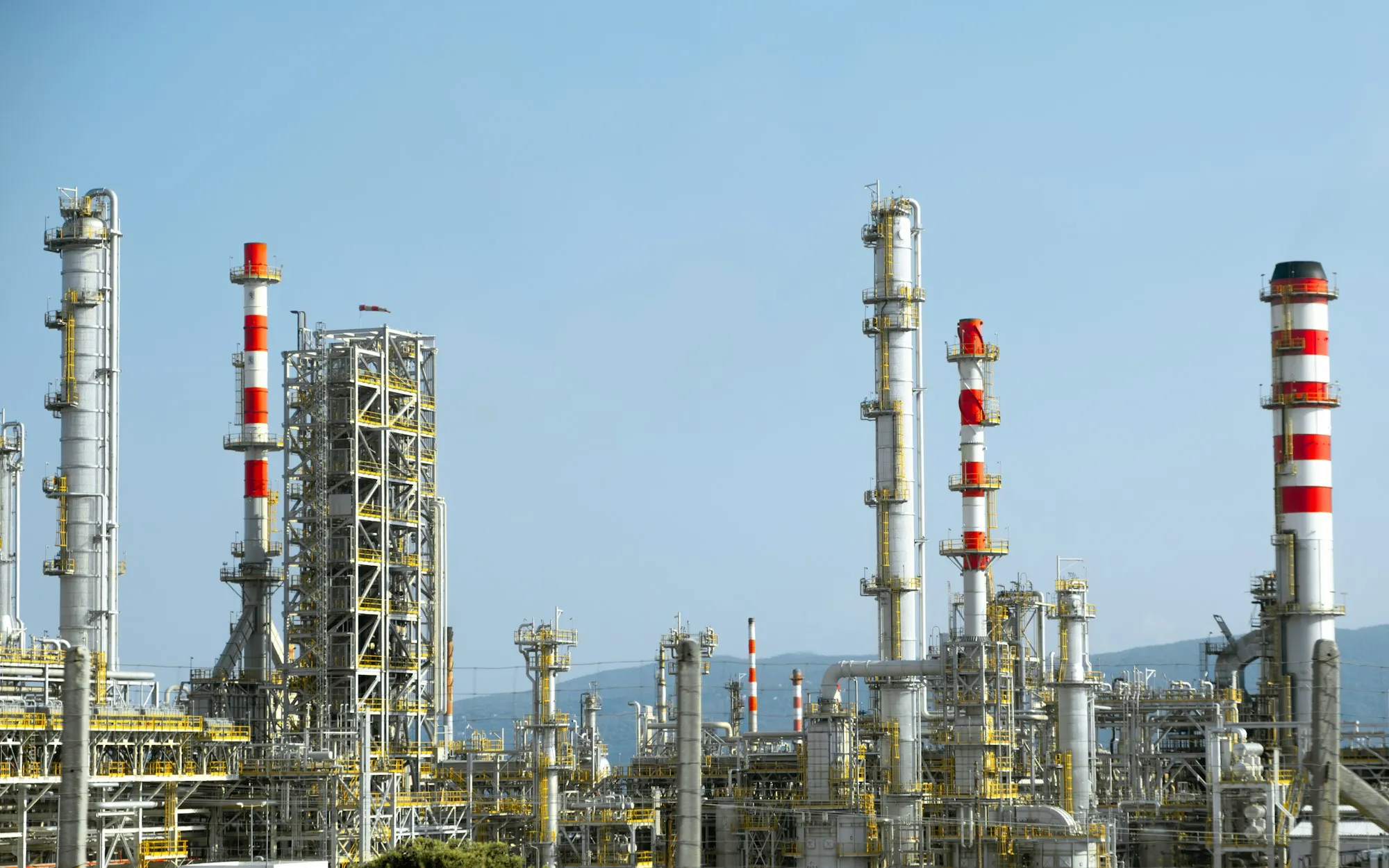 Refinery distillation columns and red-and-white stacks against a clear blue sky
